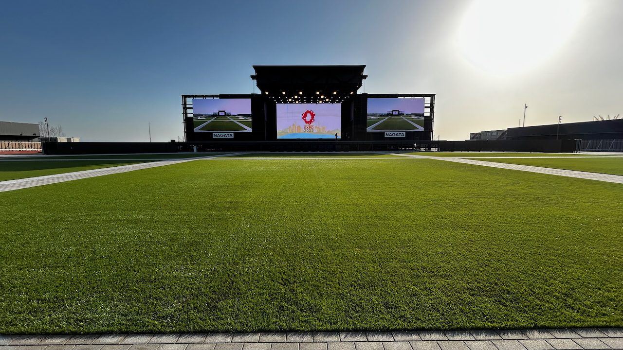 Outdoor EXPO 2025 Osaka stage with video walls, seen across the lawn