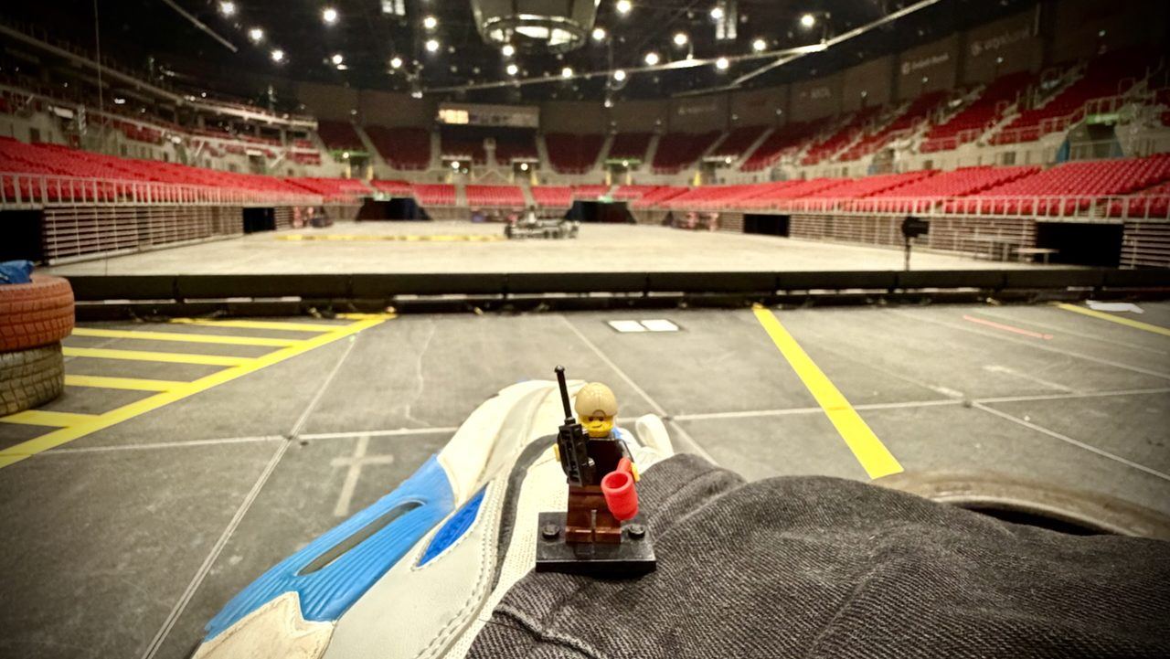 A LEGO stage-manager minifigure with a radio on an arena floor